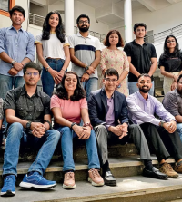 Group of people, seated and standing on stairs, posing for a group photo in a modern indoor space.