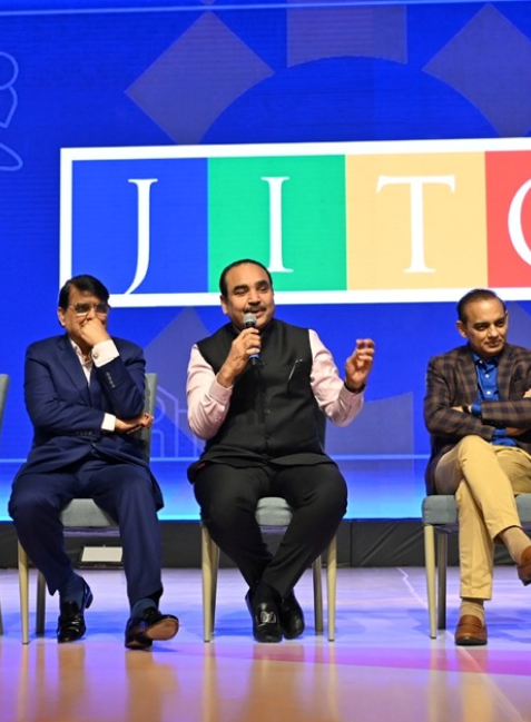 Three men on stage, one speaking with a mic, with 'JITO' displayed in the background.