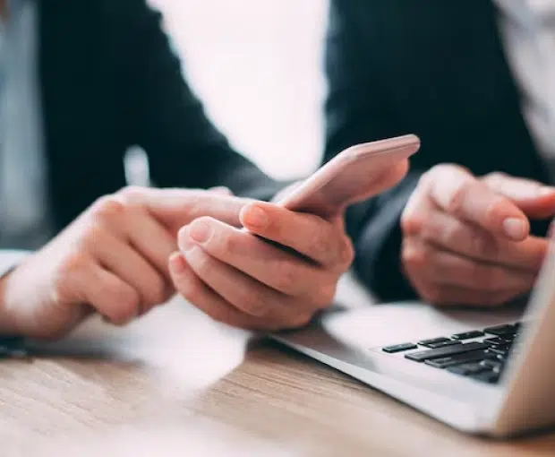 Two people in suits use smartphones and laptops during a business meeting or discussion.